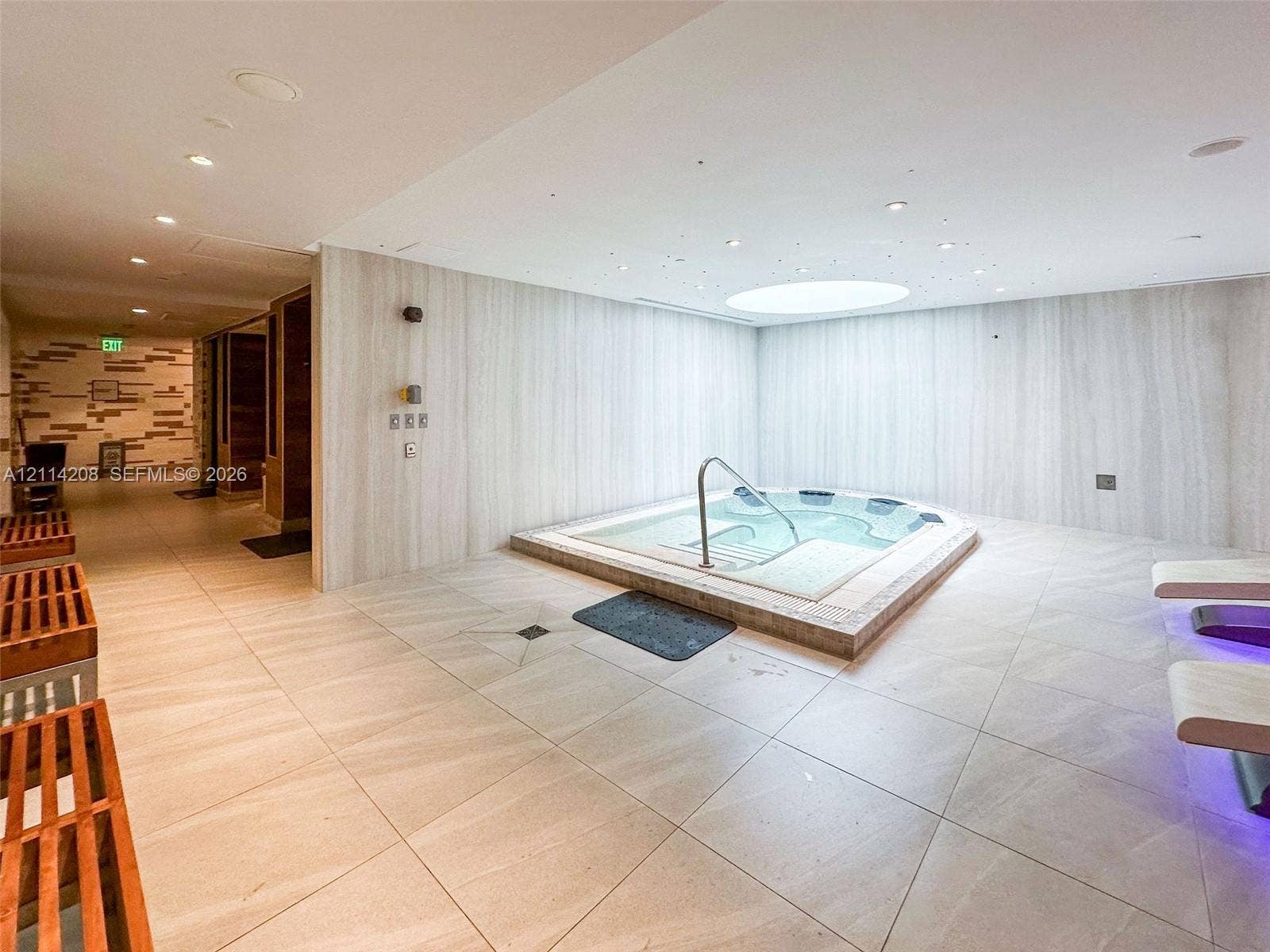 6801 Collins Avenue, #604, Miami Beach, FL 33141 Indoor spa area featuring an integrated jetted hot tub with a metal handrail, large-format tile flooring, light-toned stone-finish wall cladding, and a circular recessed ceiling skylight