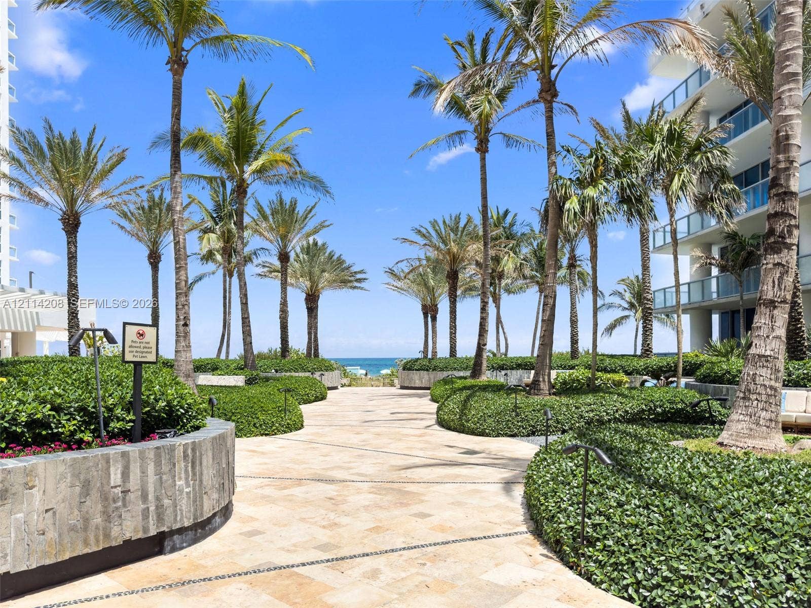 6801 Collins Avenue, #604, Miami Beach, FL 33141 Landscaped courtyard featuring stone-paved walkways, mature palm trees, stacked stone planters, and manicured shrubbery