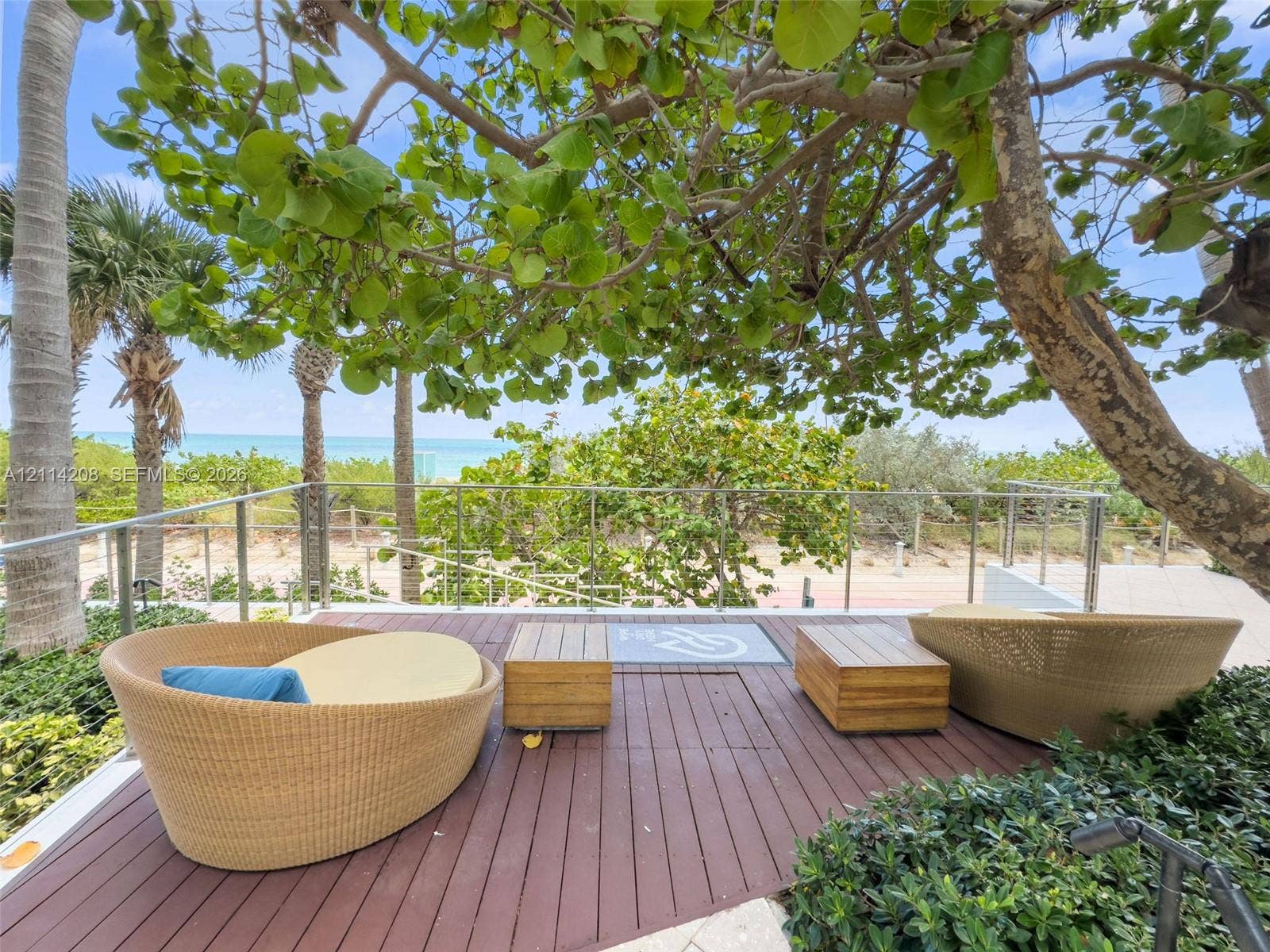 6801 Collins Avenue, #604, Miami Beach, FL 33141 Elevated wood-finish deck featuring a stainless steel cable railing system, mature sea grape trees, and open water scenery