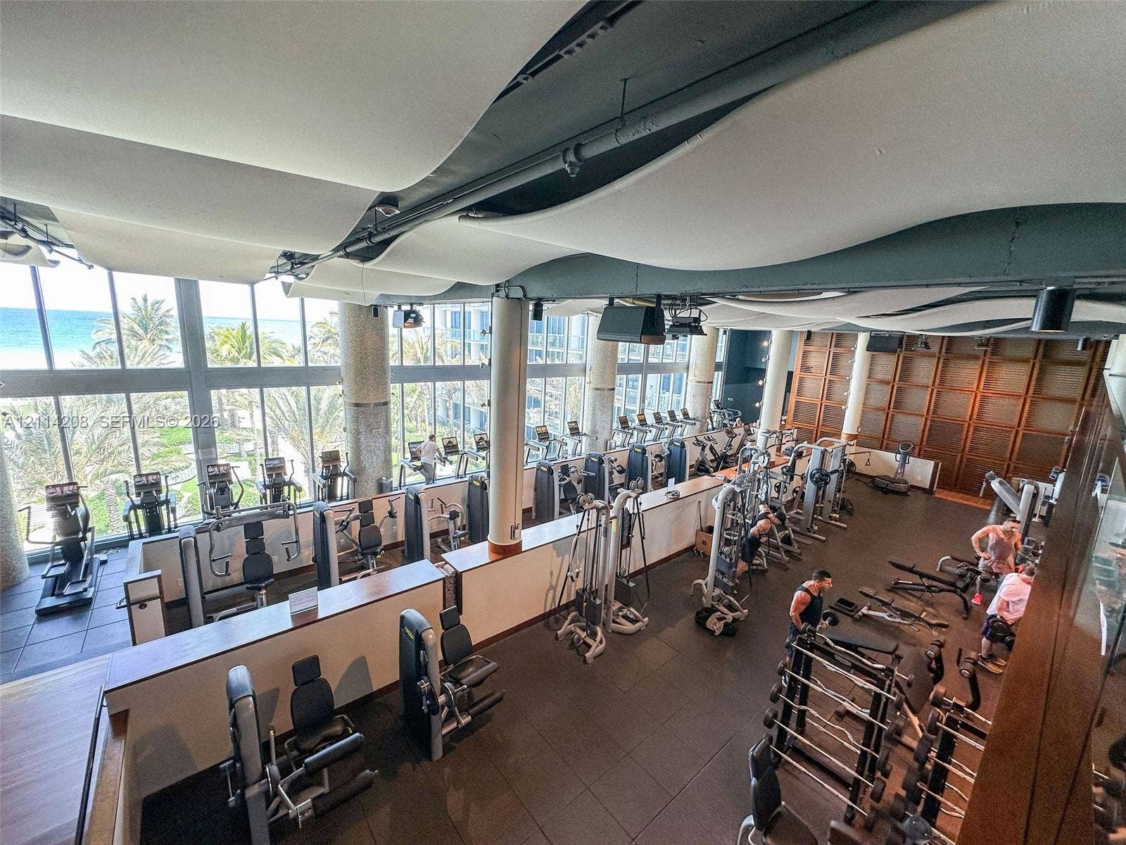 6801 Collins Avenue, #604, Miami Beach, FL 33141 Fitness center featuring expansive floor-to-ceiling windows, high-contrast wood paneling, structured fabric ceiling installations, and industrial-style exposed ductwork