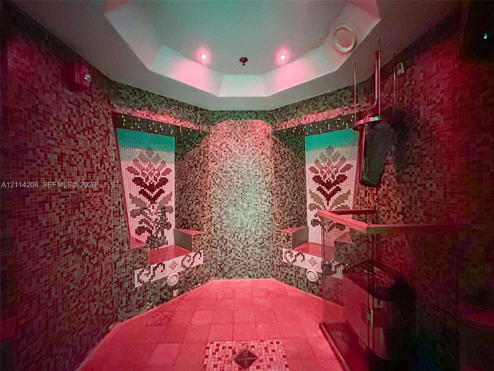 6801 Collins Avenue, #604, Miami Beach, FL 33141 Sauna featuring full-height mosaic tile walls with custom floral inlays, tiered built-in seating, an octagonal ceiling, and a glass-enclosed heater unit