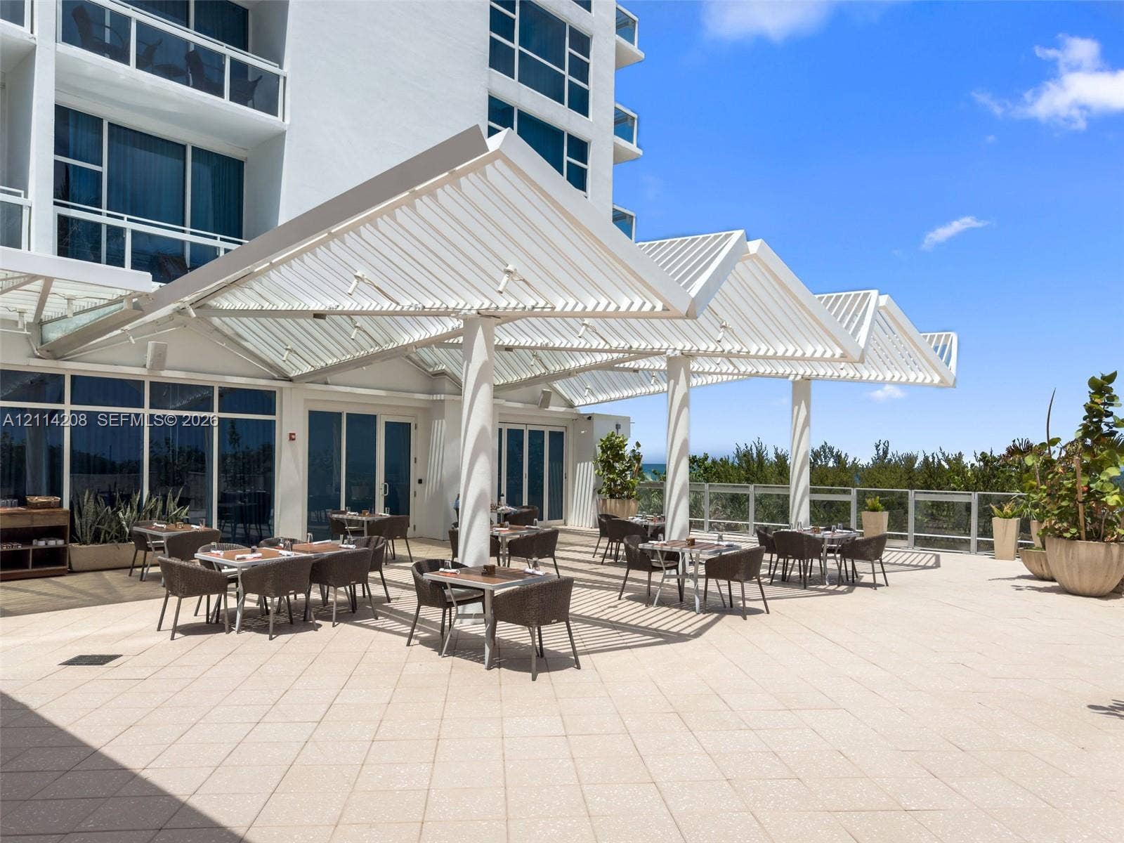 6801 Collins Avenue, #604, Miami Beach, FL 33141 Expansive outdoor terrace featuring light-toned tile flooring, a structured metal louvered canopy, and a glass-paneled perimeter railing