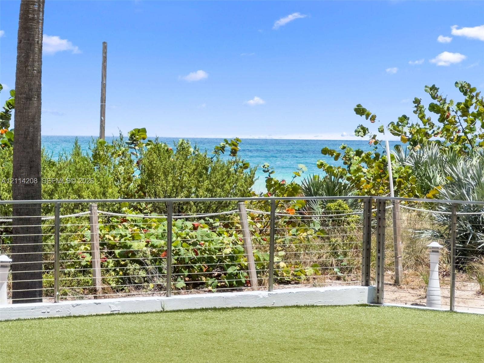 6801 Collins Avenue, #604, Miami Beach, FL 33141 Artificial turf lawn enclosed by a stainless steel cable railing system, overlooking mature coastal landscaping and the ocean