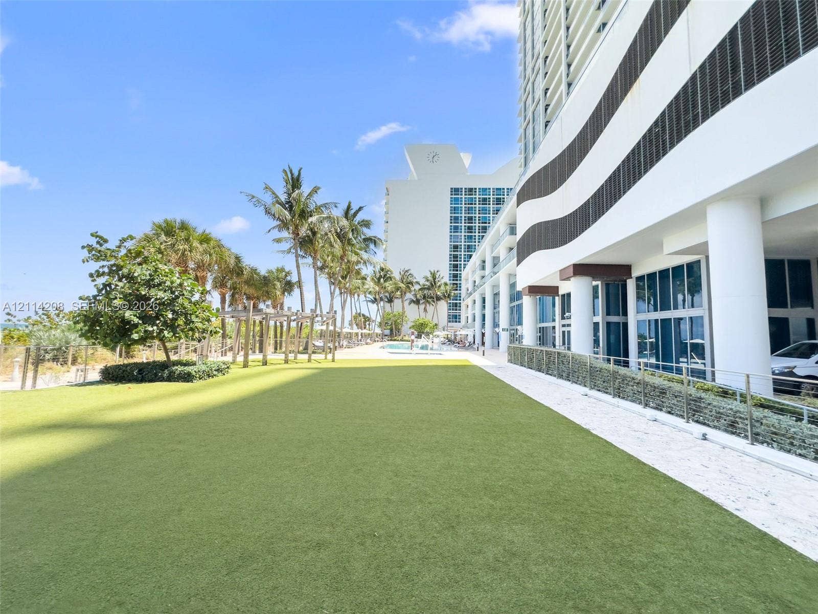 6801 Collins Avenue, #604, Miami Beach, FL 33141 Expansive artificial turf lawn featuring mature palm trees, a wooden pergola, and metal railings