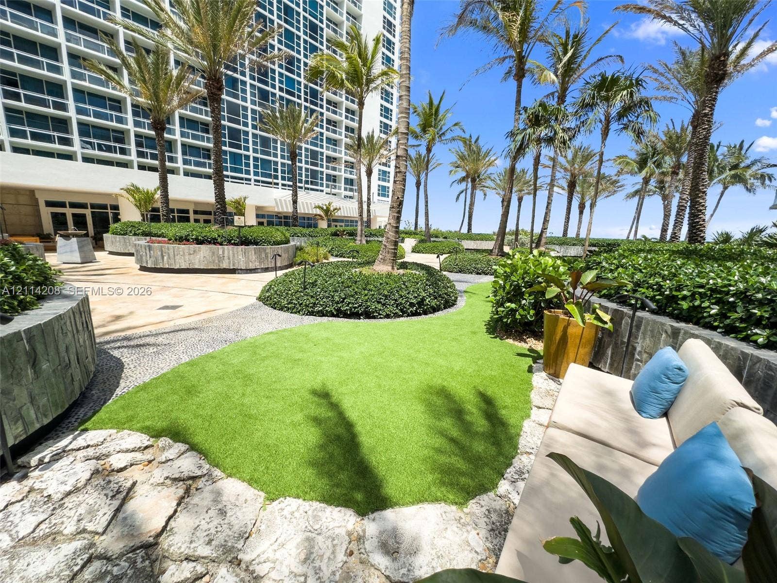 6801 Collins Avenue, #604, Miami Beach, FL 33141 Landscaped terrace featuring palm trees, synthetic grass lawn, stone-tiled hardscaping, and circular concrete planters