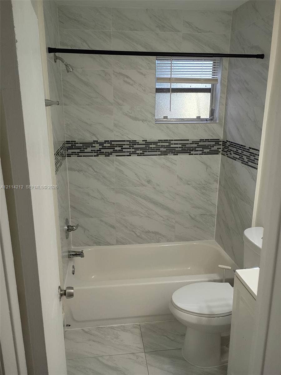 Full-height stone-finish wall tiling with integrated mosaic accent border, bathtub with chrome shower fixtures, and neutral floor tiling