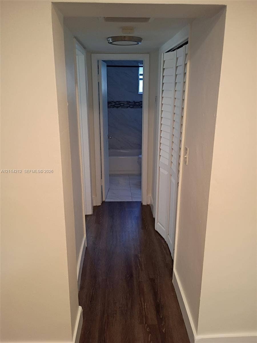 Hallway featuring wood-finish flooring, white louvered-style bi-fold closet doors, and a flush-mount ceiling light fixture
