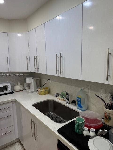 3701 N Country Club Drive, #706, Aventura, FL 33180 Kitchen featuring white high-gloss cabinetry, light-toned solid surface countertops, a stainless steel undermount sink, and brushed metal hardware