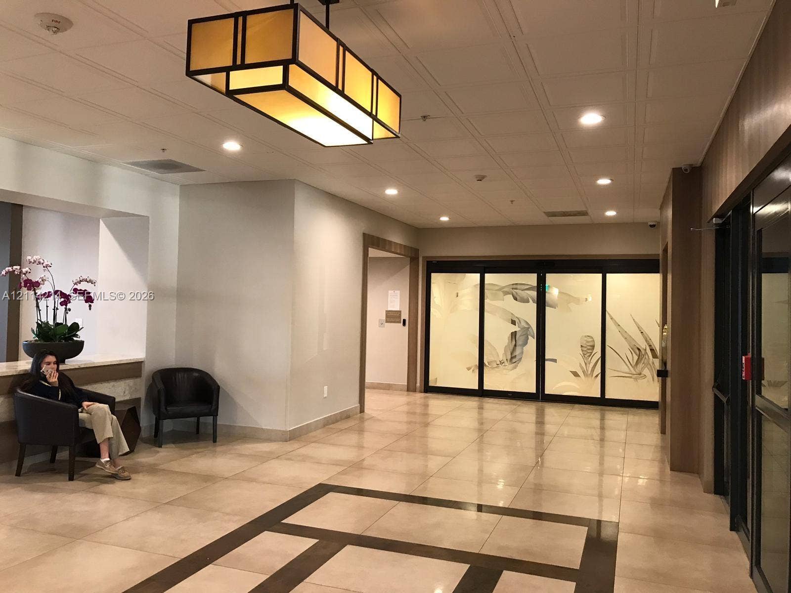 3701 N Country Club Drive, #706, Aventura, FL 33180 Lobby featuring large-format tile flooring with inlaid geometric borders, rectangular pendant lighting, and decorative frosted glass panels with etched leaf motifs