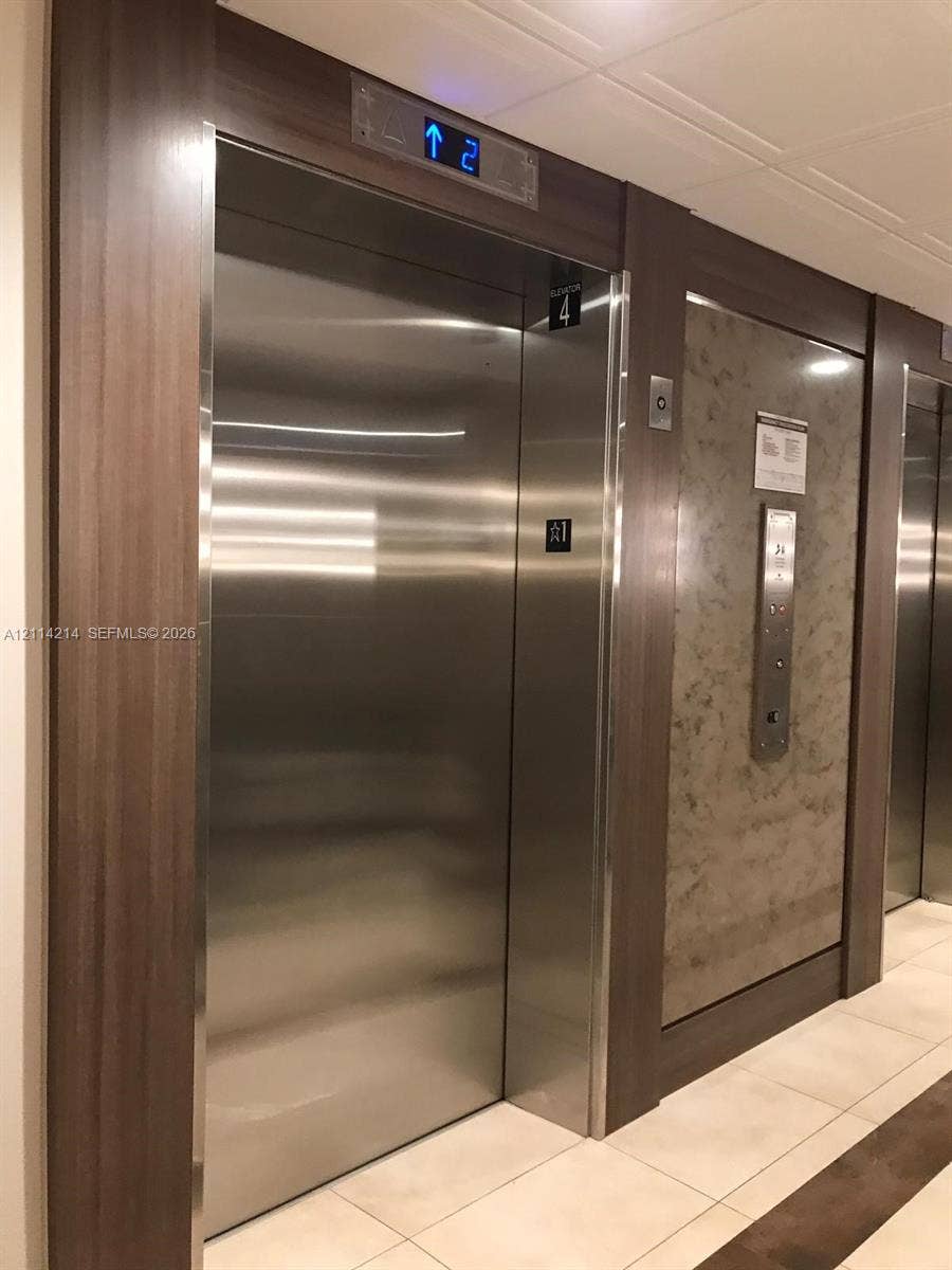 3701 N Country Club Drive, #706, Aventura, FL 33180 Elevator access featuring brushed stainless steel doors, floor-level digital display, wood-finish trim, and decorative stone-patterned paneling