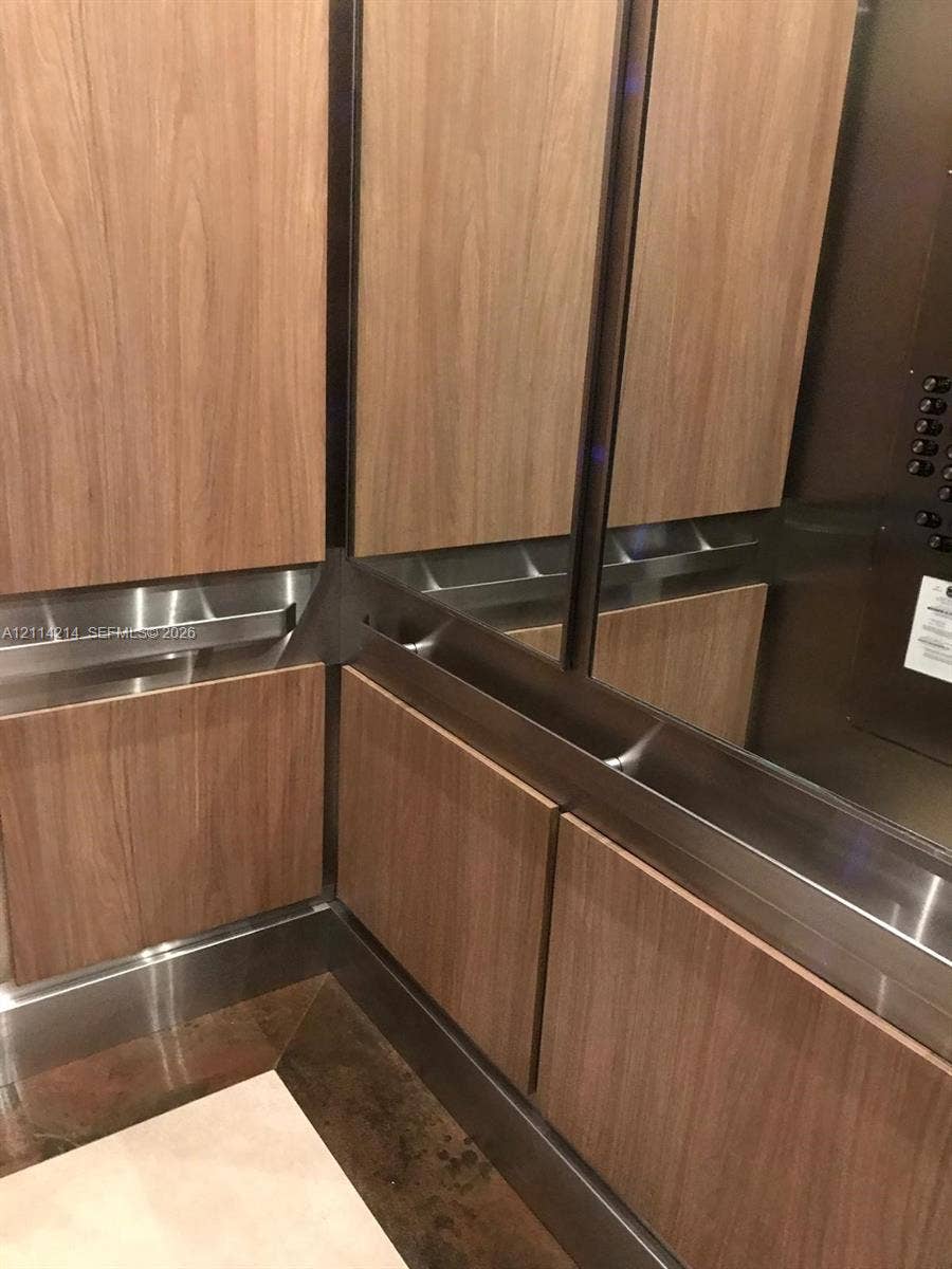 3701 N Country Club Drive, #706, Aventura, FL 33180 Elevator interior featuring wood-finish paneling, brushed metallic trim, and integrated stainless steel handrails