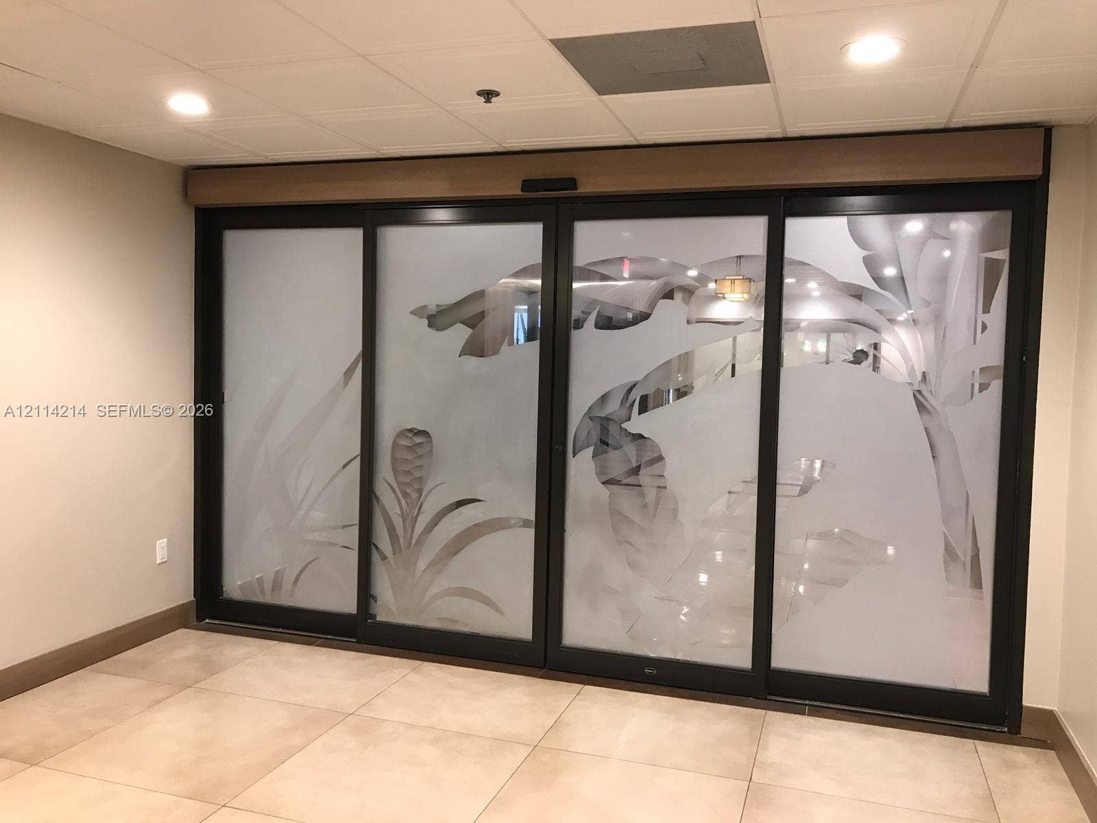 3701 N Country Club Drive, #706, Aventura, FL 33180 Sliding glass doors featuring black frames and frosted botanical-patterned panels, paired with large-format neutral floor tiling and recessed ceiling lighting