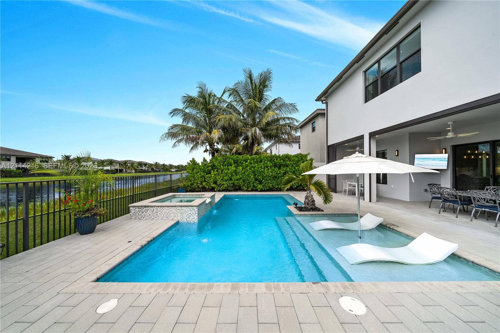17085 Teton River Road, Boca Raton, FL 33496 Rear patio featuring a swimming pool with a built-in spa, a tanning ledge, light-toned paver decking, and metal perimeter fencing overlooking a waterway