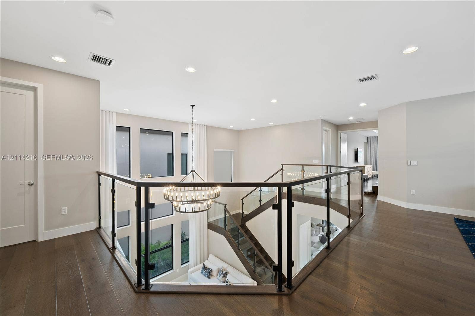 17085 Teton River Road, Boca Raton, FL 33496 Open mezzanine landing featuring wood-finish flooring, glass panel railing with dark metal framing, recessed lighting, and a multi-tiered circular chandelier