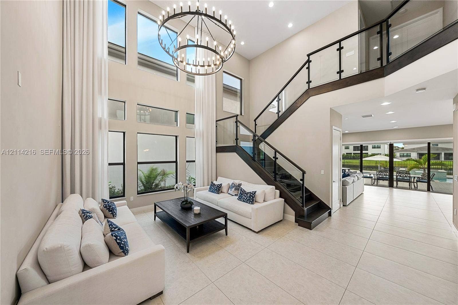 17085 Teton River Road, Boca Raton, FL 33496 Two-story foyer featuring a floor-to-ceiling window wall, a modern multi-tier circular chandelier, and a custom staircase with glass panels and dark wood-finish railings