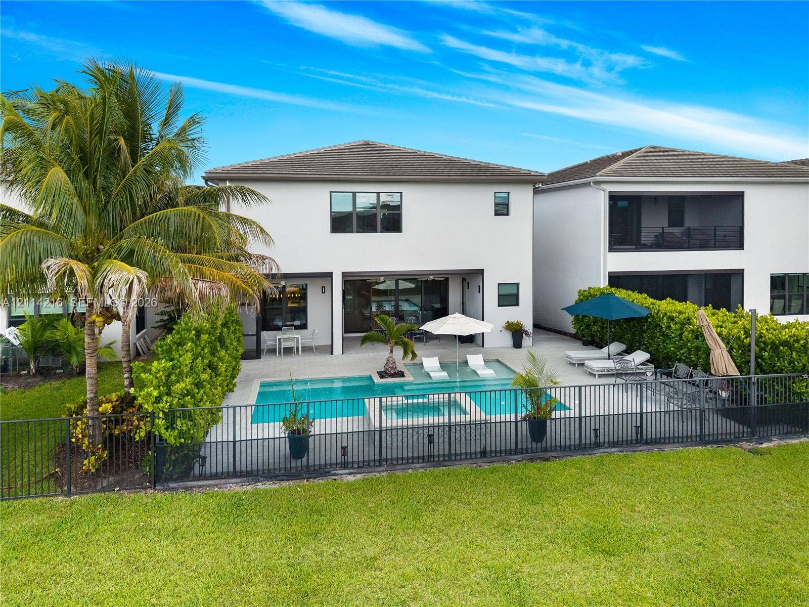 17085 Teton River Road, Boca Raton, FL 33496 Rear exterior featuring a swimming pool with integrated spa, a paver patio, metal perimeter fencing, and established privacy hedges