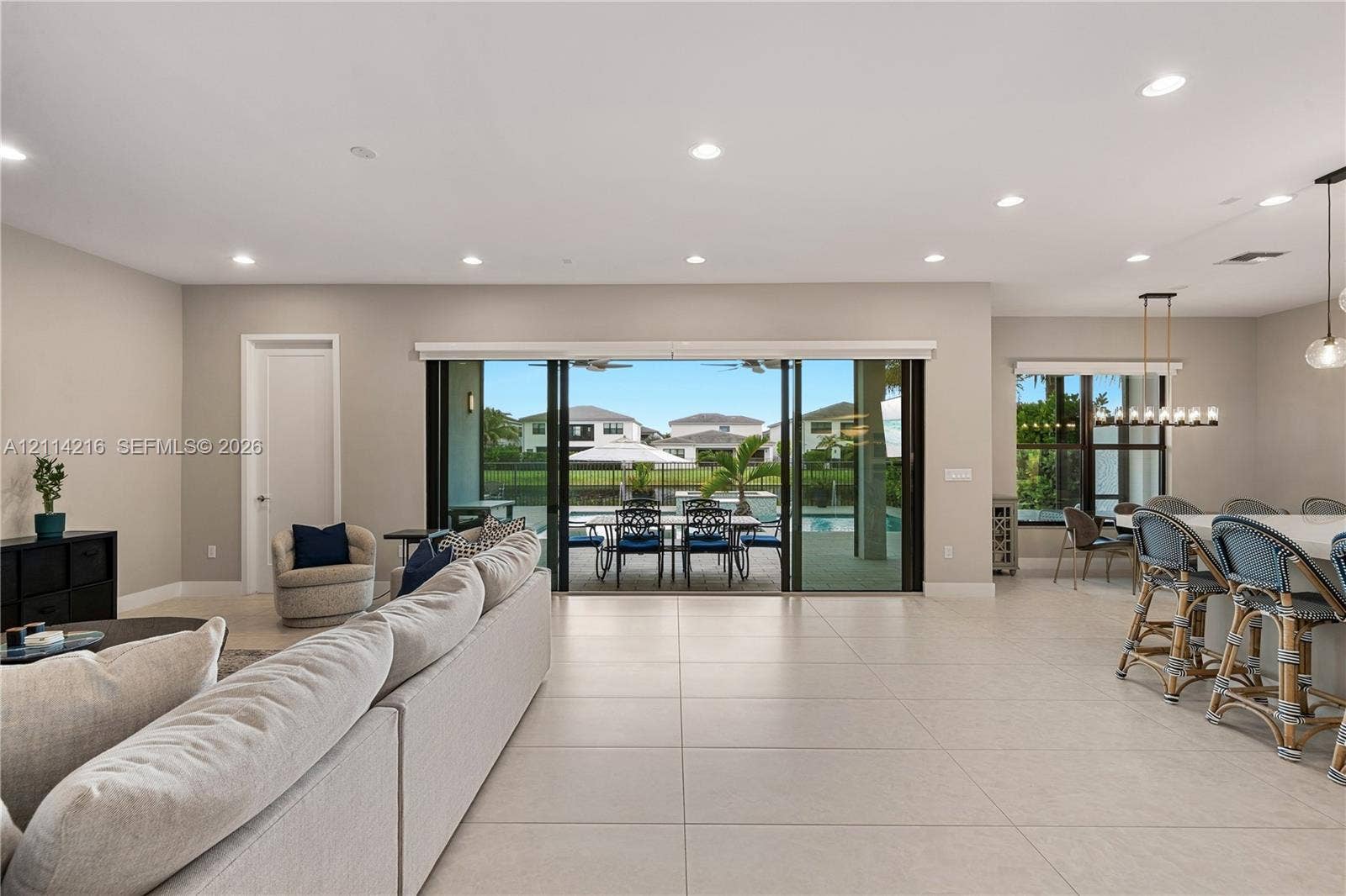 17085 Teton River Road, Boca Raton, FL 33496 Open-concept interior featuring large-format tile flooring, recessed ceiling lighting, and expansive multi-panel sliding glass doors opening to a covered patio