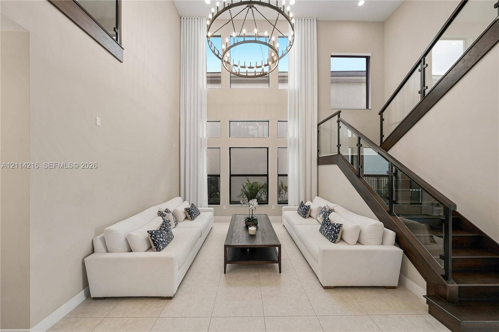 17085 Teton River Road, Boca Raton, FL 33496 Two-story height ceiling with expansive windows, custom iron-frame chandelier, and staircase featuring dark wood finishes and glass railing panels