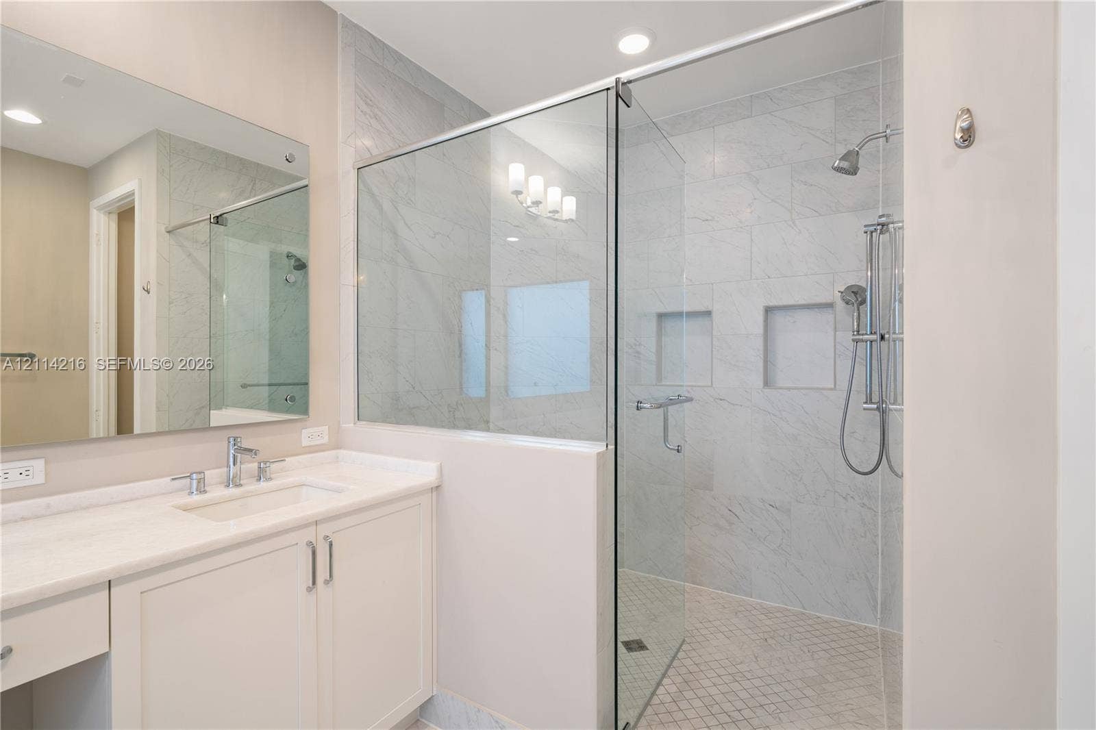 17085 Teton River Road, Boca Raton, FL 33496 Bathroom featuring a vanity with a light-toned countertop, undermount sink, and integrated cabinetry, paired with a walk-in shower enclosed by glass panels, stone-finish wall tiling, dual recessed niches, and a handheld shower fixture