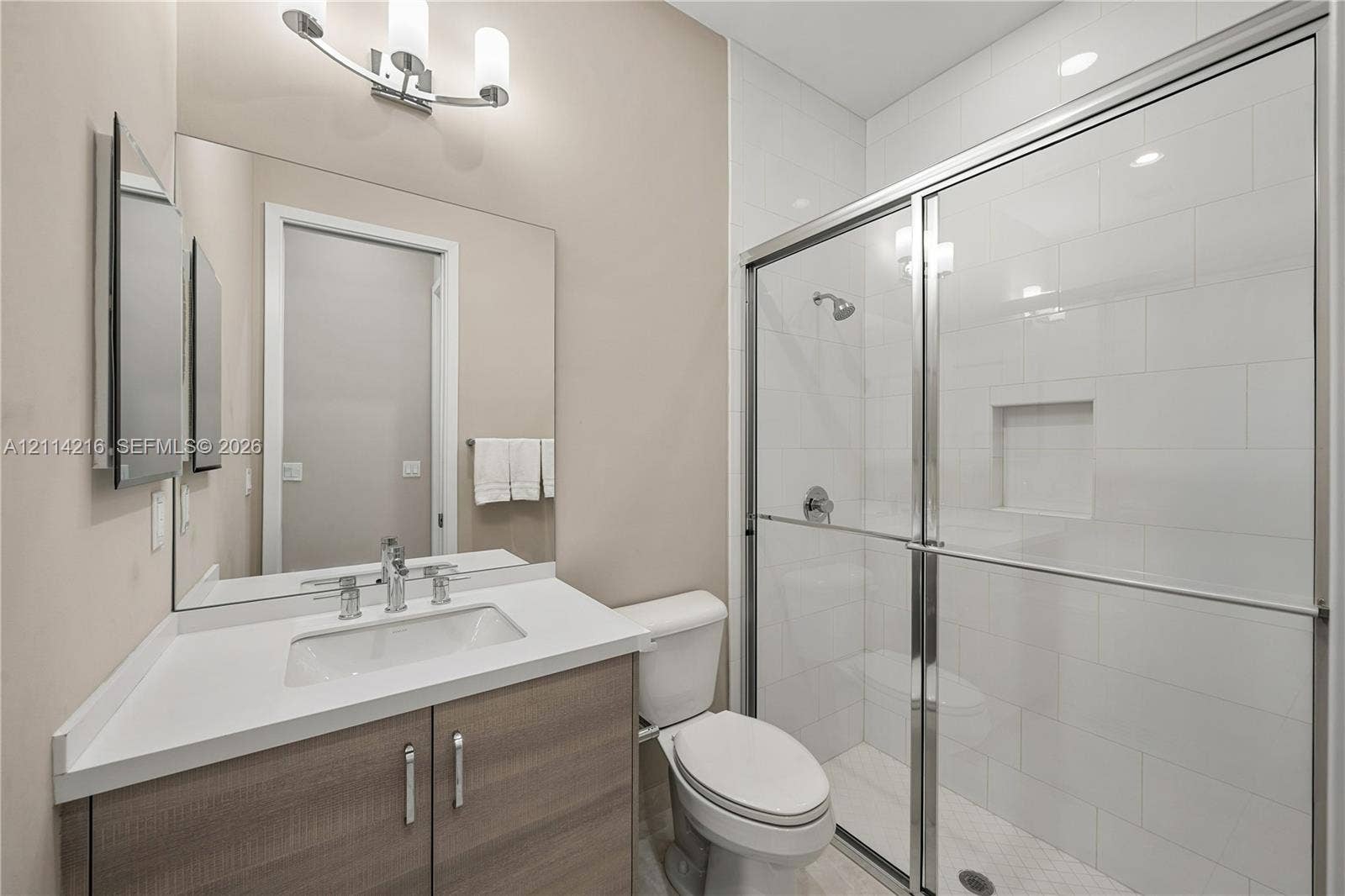 17085 Teton River Road, Boca Raton, FL 33496 Bathroom featuring a wood-finish vanity with a stone countertop, an integrated rectangular sink, a glass-enclosed shower with subway tile surround, and an expansive wall-mounted mirror