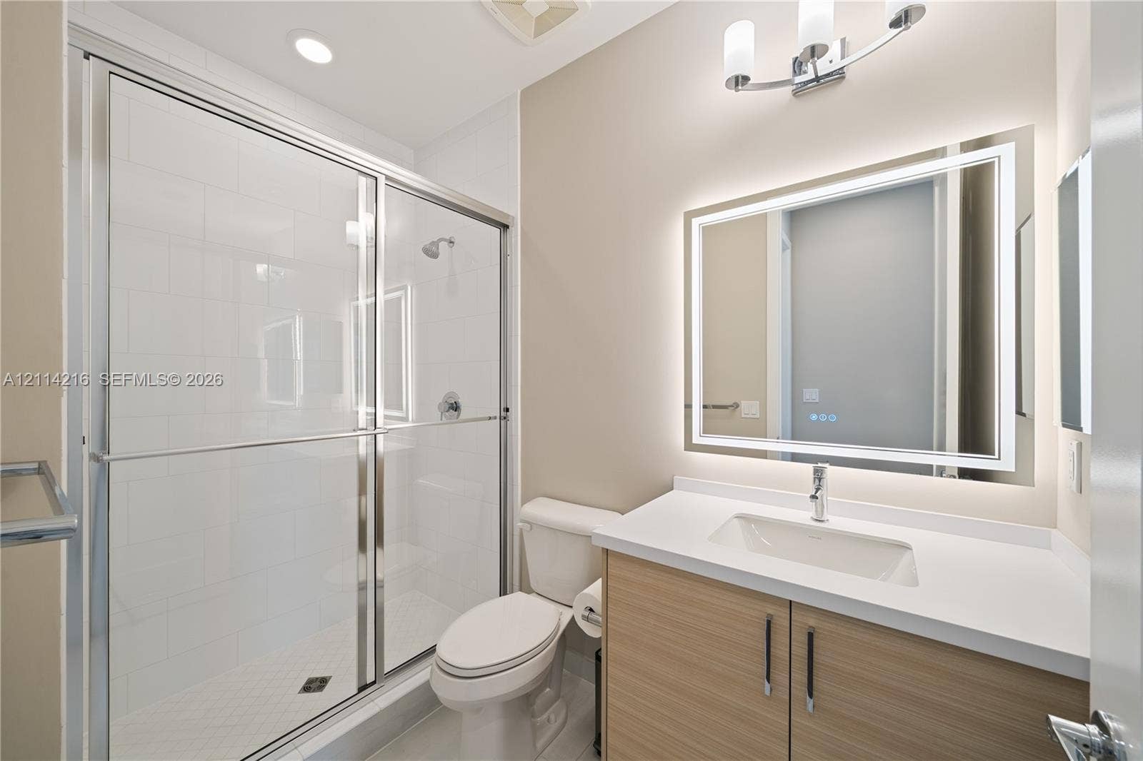 17085 Teton River Road, Boca Raton, FL 33496 Bathroom featuring a walk-in shower with a glass enclosure, wood-finish vanity with a stone countertop, integrated undermount sink, and a modern LED-backlit mirror