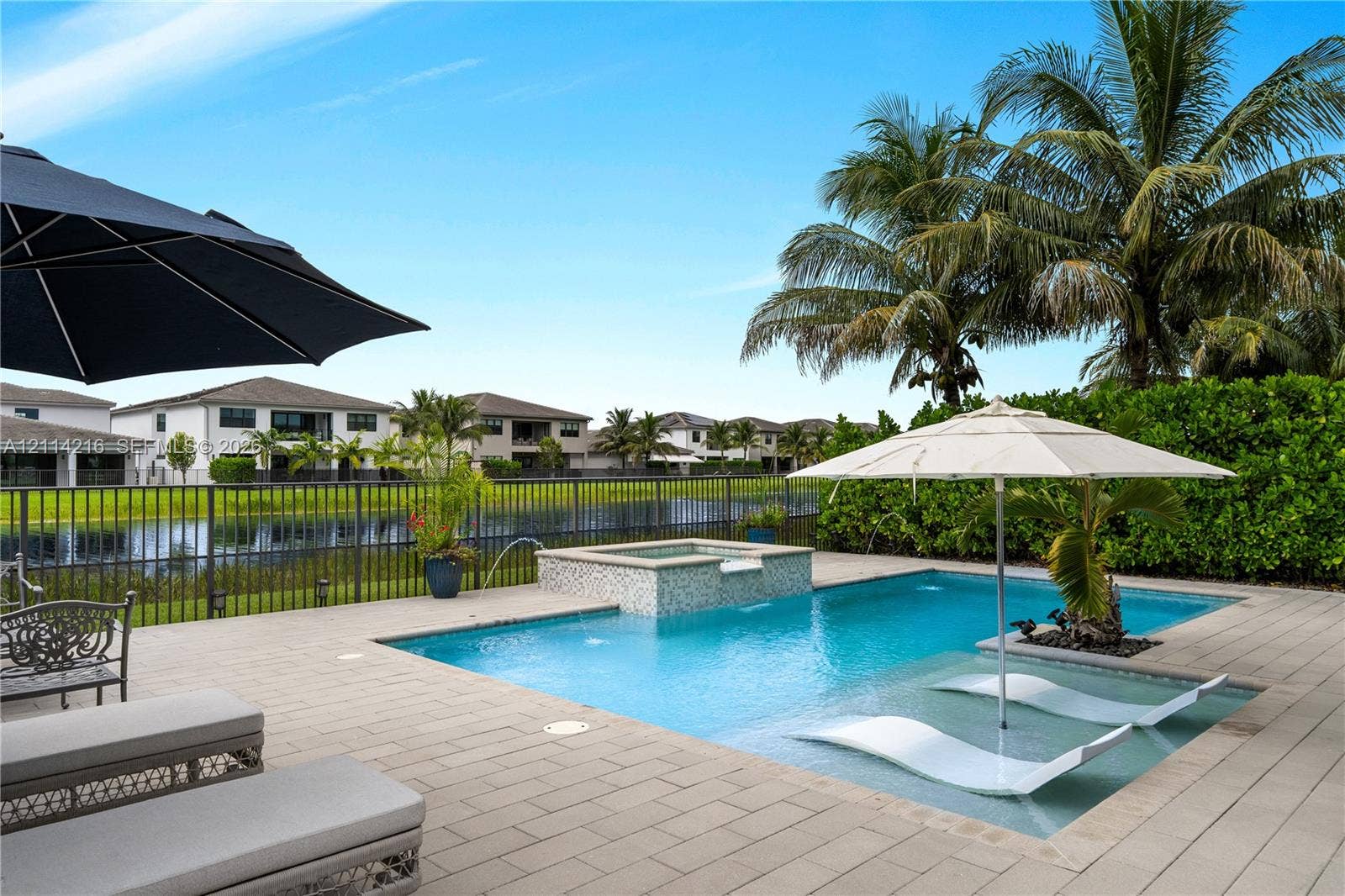17085 Teton River Road, Boca Raton, FL 33496 In-ground swimming pool featuring a built-in spillover spa, tanning ledge, stone-finish paver deck, and metal perimeter fencing