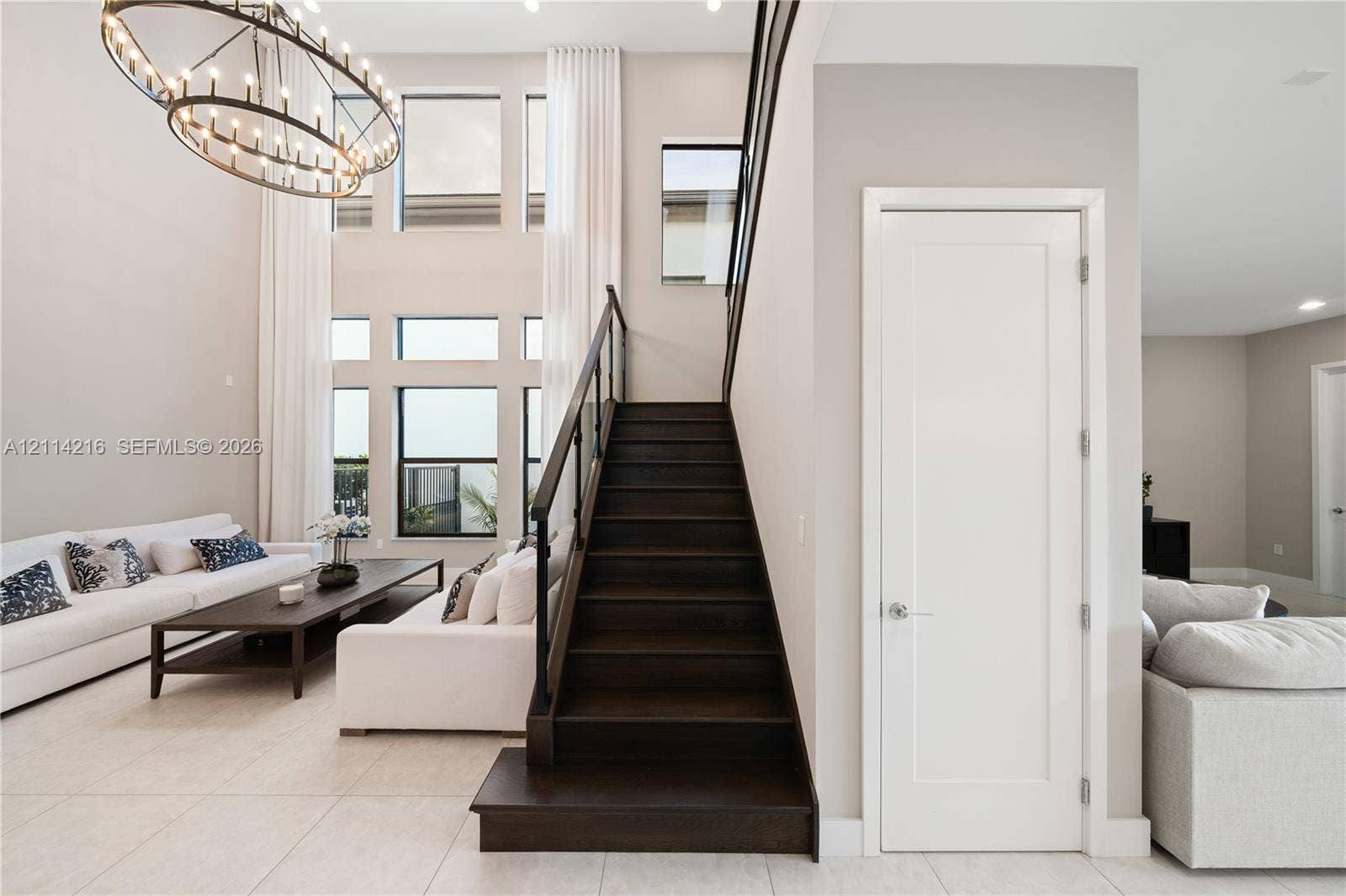 17085 Teton River Road, Boca Raton, FL 33496 Double-height ceiling, large multi-pane windows, statement ring chandelier, staircase with wood-finish treads and a dark metal railing, and light-toned tile flooring