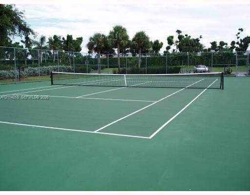 1116 Meadows Circle, #1116, Boynton Beach, Boynton Beach, FL 33436 Private tennis court featuring a green surface, court markings, perimeter chain-link fencing, and mature palm trees