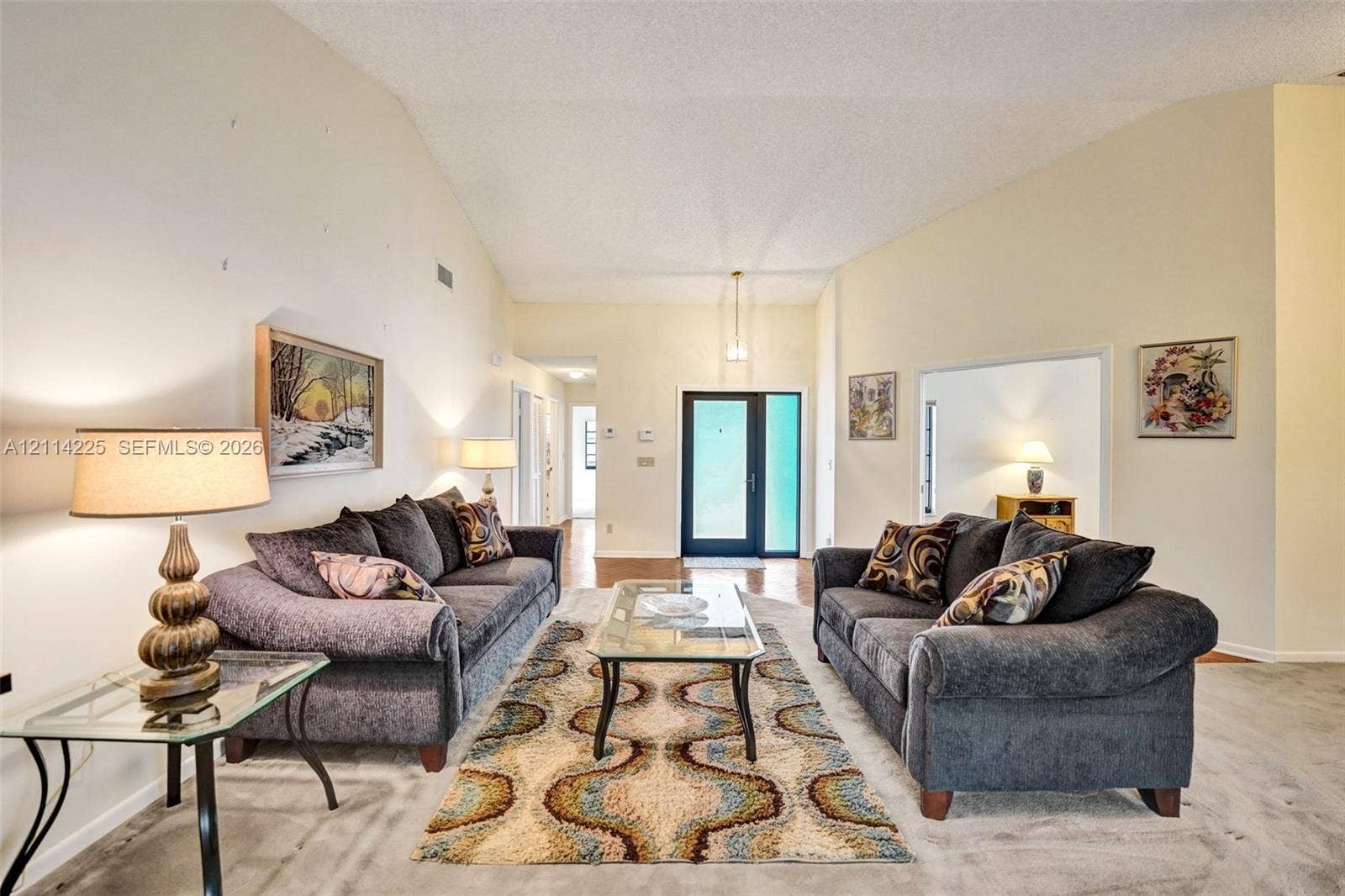 5741 SW 88th Terrace, Cooper City, FL 33328 Living area featuring vaulted ceilings, a glass-panel entry door, and neutral wall tones