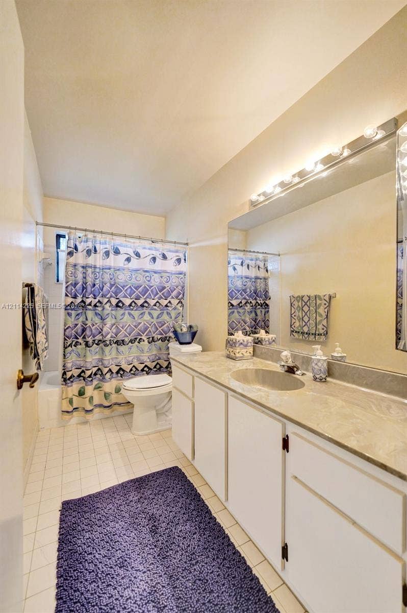 5741 SW 88th Terrace, Cooper City, FL 33328 Full-width vanity featuring a stone-composite countertop with an integrated basin, white shaker-style cabinetry, large wall-mounted mirror, and multi-bulb fixture
