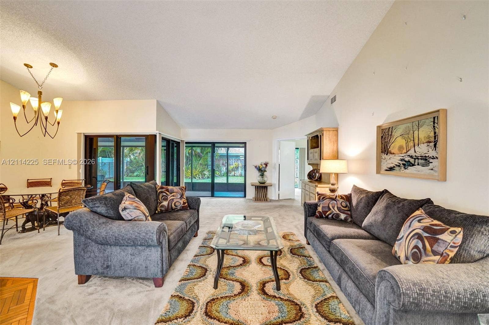 5741 SW 88th Terrace, Cooper City, FL 33328 Vaulted ceilings, expansive sliding glass doors, neutral carpeting, and a multi-arm chandelier featuring classic candle-style lighting