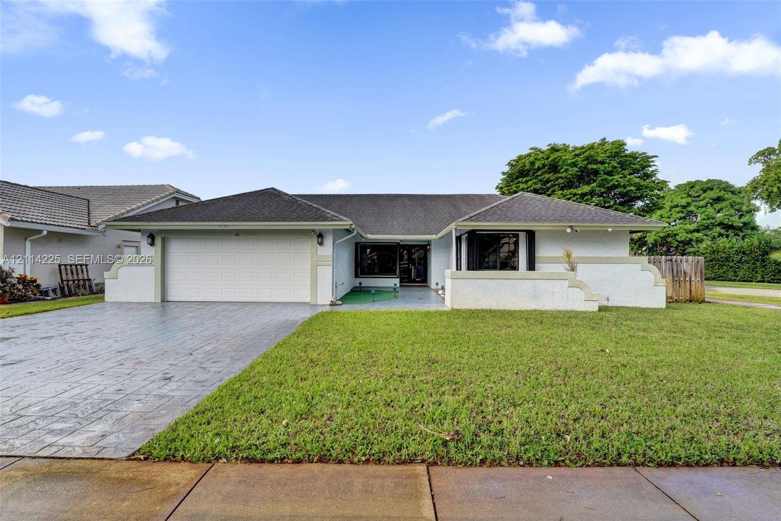 5741 SW 88th Terrace, Cooper City, FL 33328 Single-story residence featuring a painted masonry exterior, hipped roofline, integrated two-car garage, and a stamped concrete driveway