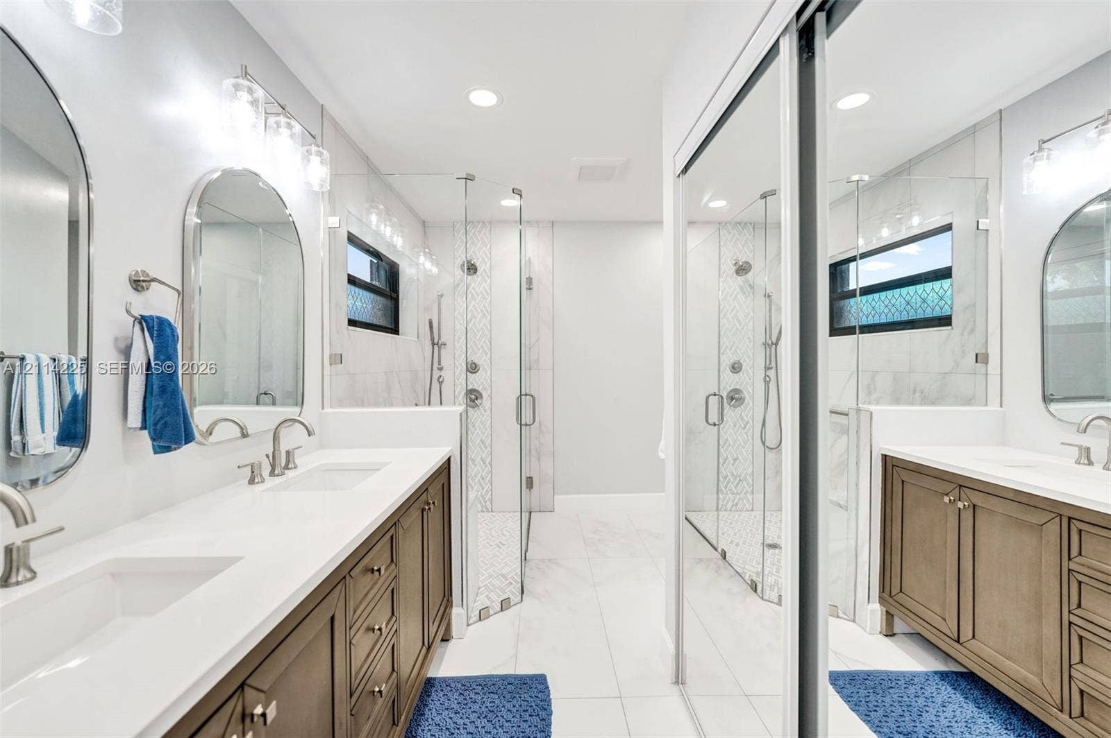 5741 SW 88th Terrace, Cooper City, FL 33328 Dual wood-finish vanities with quartz countertops and undermount sinks, arched wall mirrors, and a walk-in glass-enclosed shower featuring stone tile accents and dual showerheads