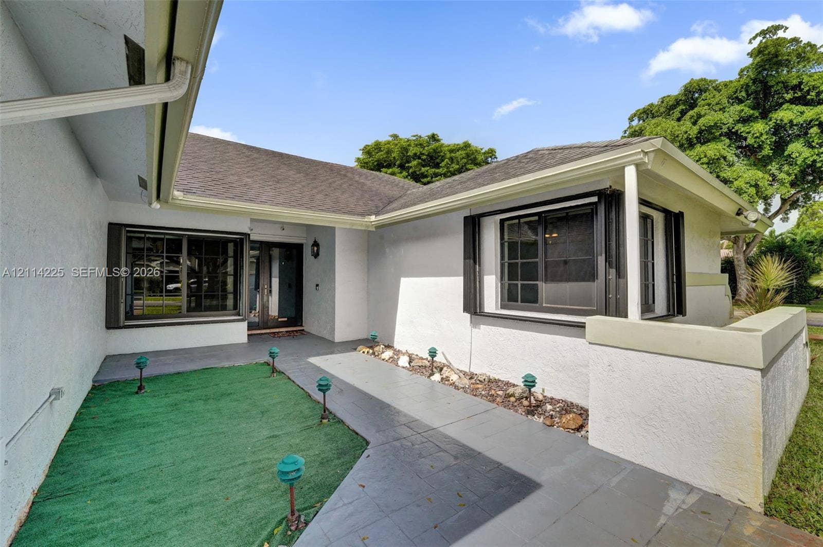 5741 SW 88th Terrace, Cooper City, FL 33328 Stucco exterior featuring an asphalt shingle roof, dark-framed grid windows, a covered entryway, and a paved walkway with integrated low-voltage lighting