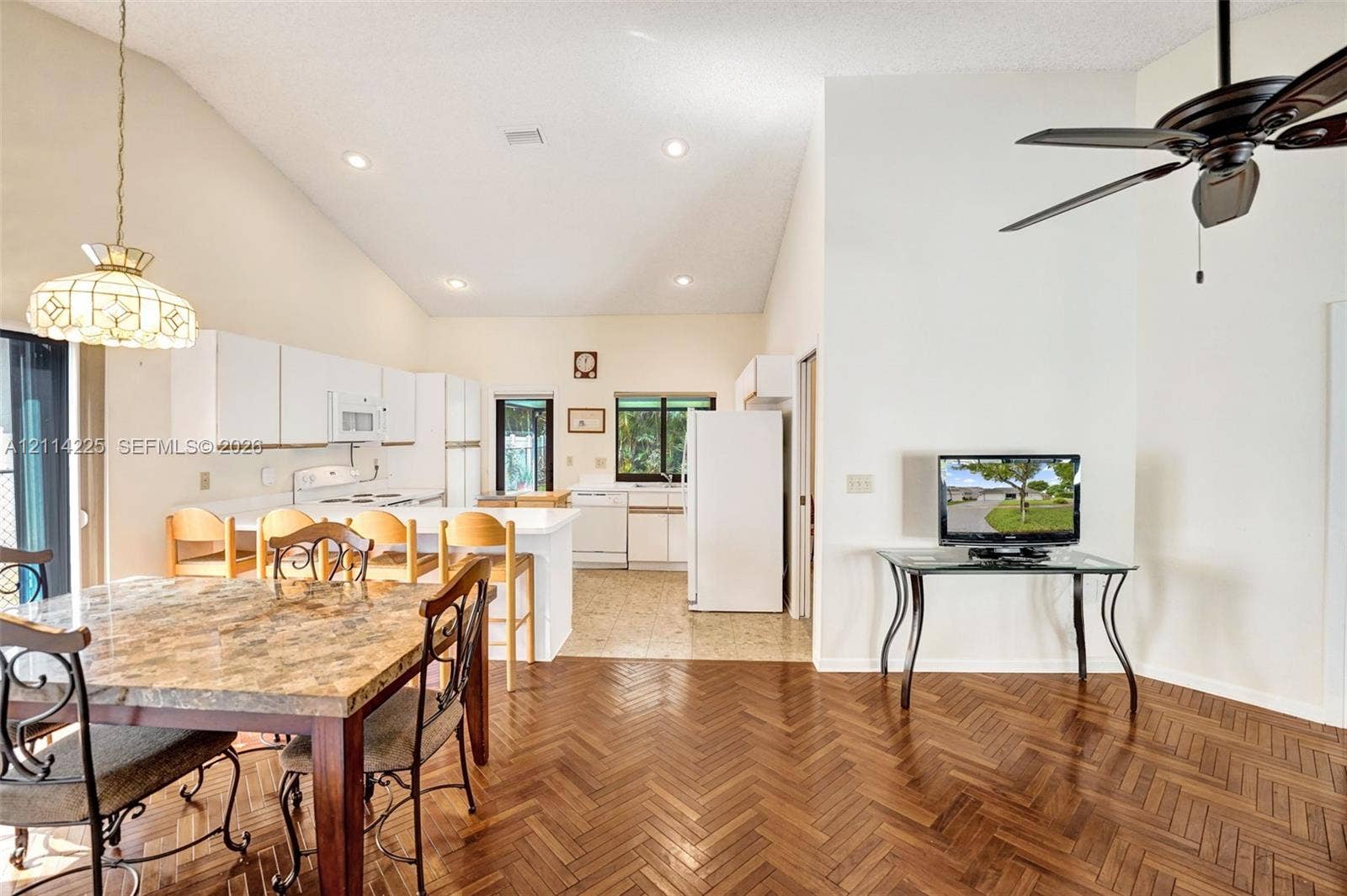 5741 SW 88th Terrace, Cooper City, FL 33328 Open-concept interior featuring vaulted ceilings, herringbone-patterned wood flooring, recessed lighting, and a breakfast bar with built-in cabinetry