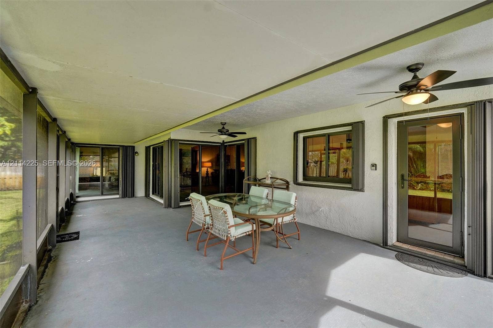 5741 SW 88th Terrace, Cooper City, FL 33328 Screened-in patio featuring a concrete floor, multiple sliding glass door entries, and dual overhead ceiling fans