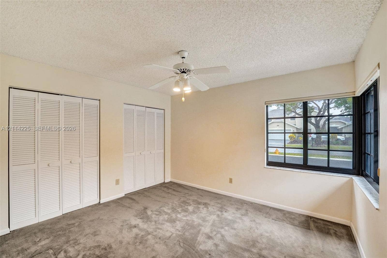 5741 SW 88th Terrace, Cooper City, FL 33328 Room featuring neutral carpeting, dual white louvered closet doors, a white ceiling fan with integrated lighting, and a multi-pane corner window