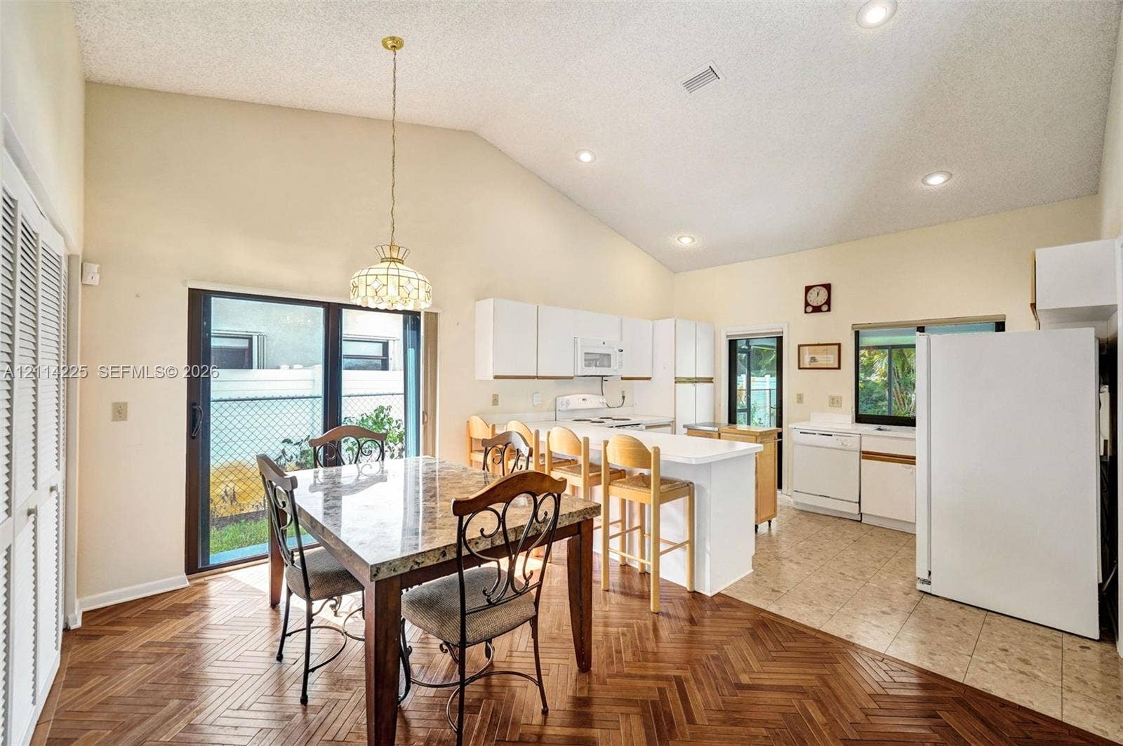 5741 SW 88th Terrace, Cooper City, FL 33328 Open-concept kitchen and dining area featuring vaulted ceilings, herringbone-pattern wood-finish flooring, a breakfast bar, and sliding glass doors