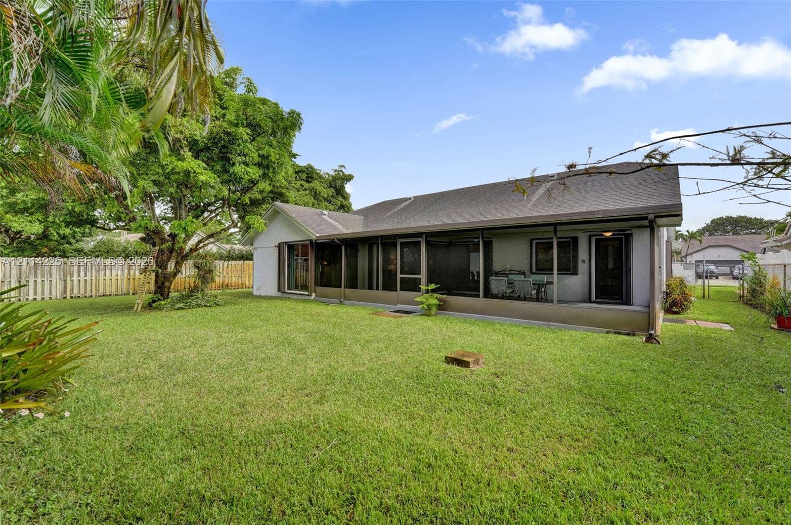 5741 SW 88th Terrace, Cooper City, FL 33328 Spacious backyard featuring a manicured lawn, mature trees, and perimeter wood-style fencing, complete with a screened-in rear porch