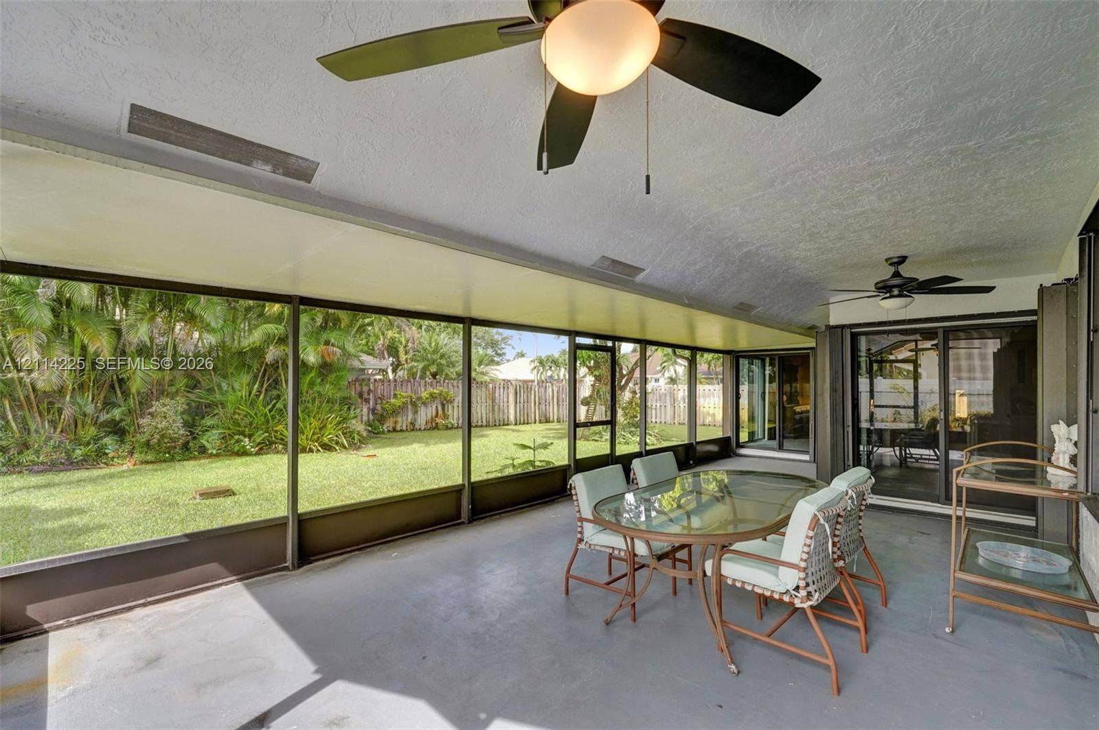 5741 SW 88th Terrace, Cooper City, FL 33328 Screened-in lanai featuring a solid ceiling with dual overhead fans, concrete flooring, and sliding glass door access to the backyard