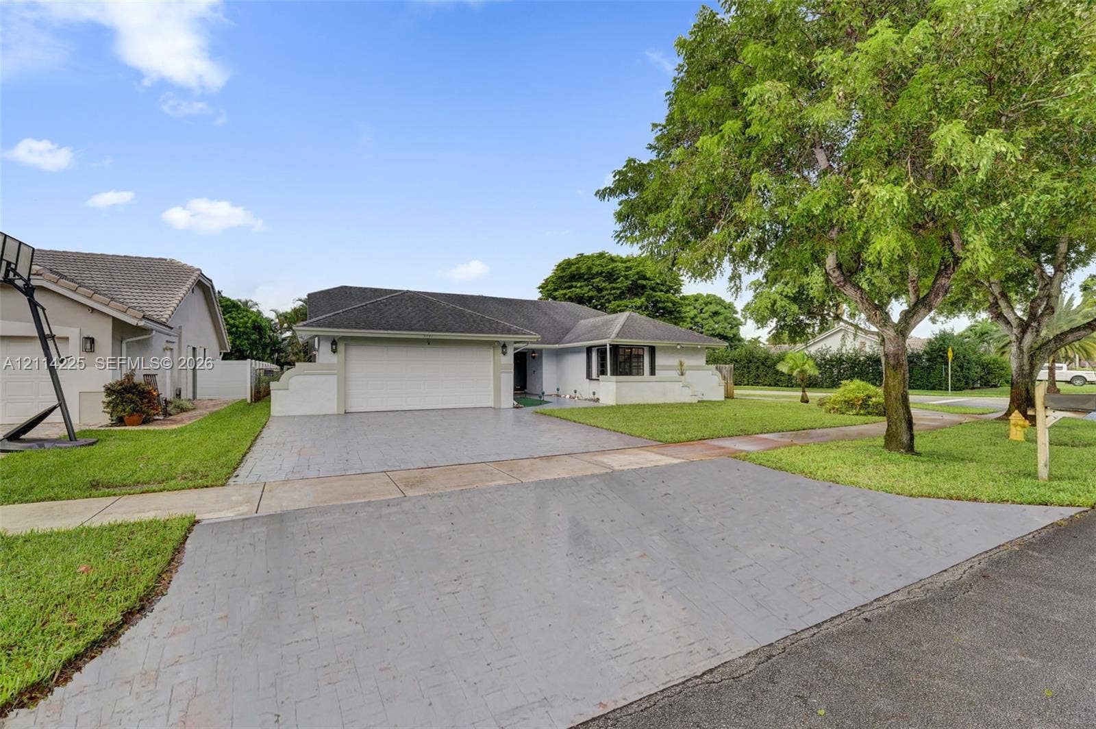 5741 SW 88th Terrace, Cooper City, FL 33328 Single-story exterior featuring a textured concrete driveway, attached two-car garage, bay window, and mature landscaping