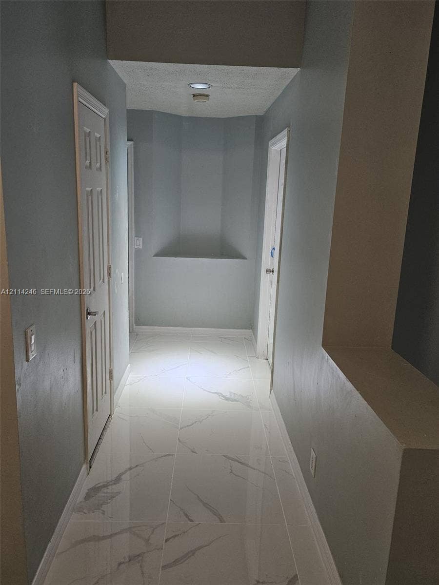 Hallway featuring large-format tile flooring with a veined finish, recessed wall niches, and paneled interior doors