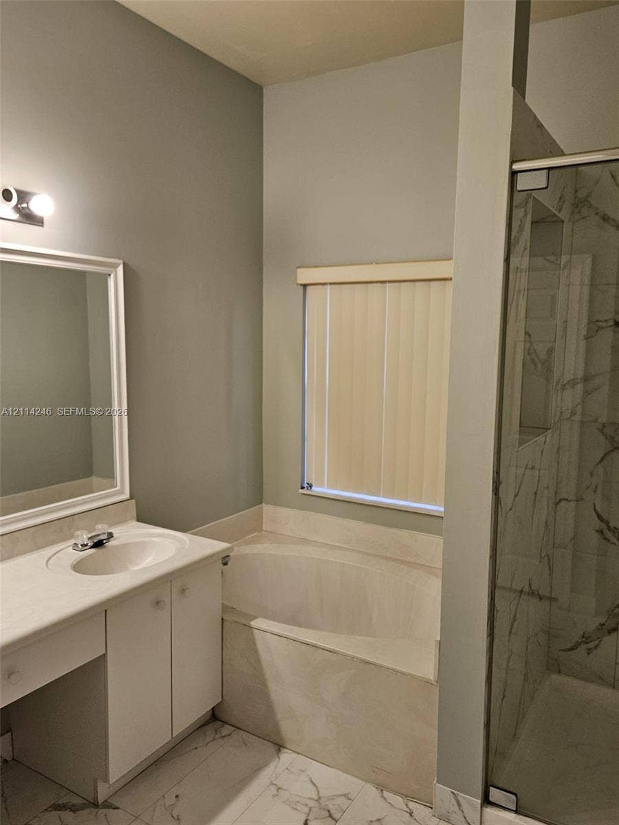 Vanity with integrated sink and countertop, soaking tub with tile surround, glass-enclosed shower with tiled walls, and large-format tile flooring