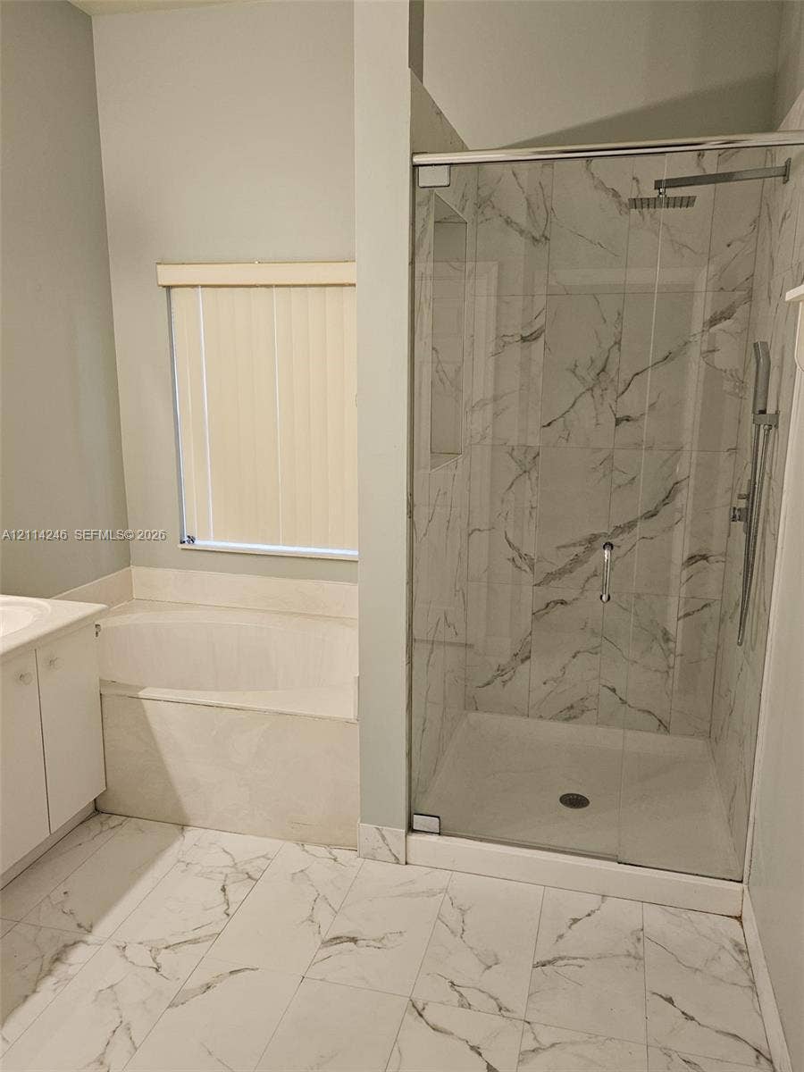 Walk-in shower with stone-finish tile surround, ceiling-mounted rainfall shower head, glass enclosure, built-in soaking tub, and large-format tile flooring