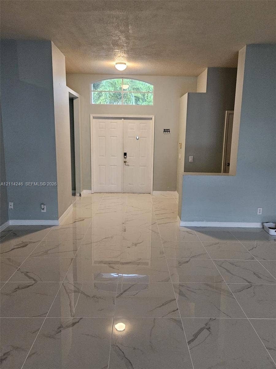 Entryway featuring large-format tile flooring with a neutral veined pattern, double front doors, and a semi-circular transom window
