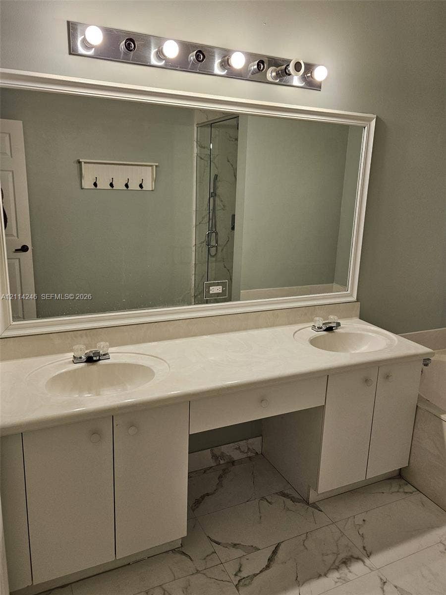 Dual-sink vanity with white cabinetry, integrated stone-finish countertop, full-width mirror, and multi-bulb vanity lighting, accented by large-format floor tiling