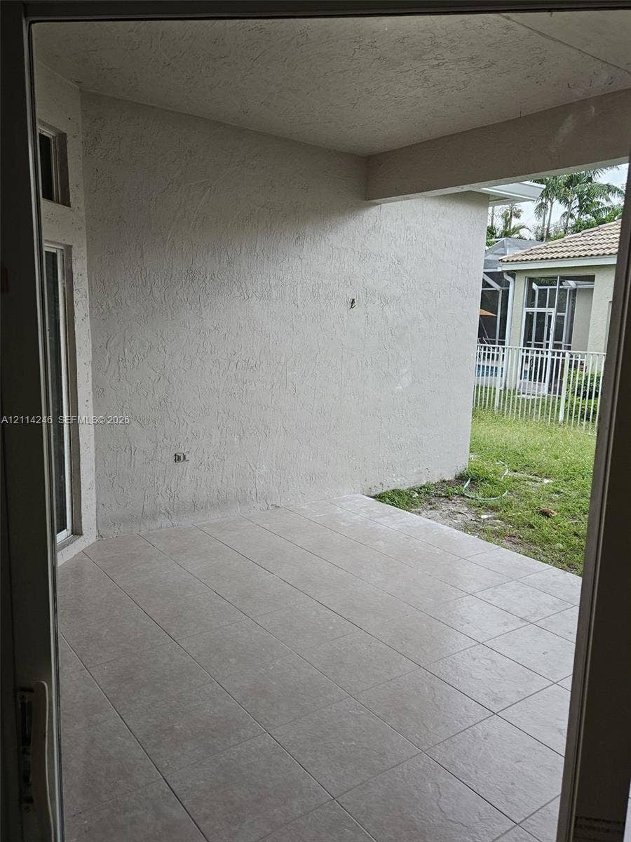 Covered concrete patio featuring large-format ceramic floor tiles, textured stucco walls, and an open entryway to the exterior grounds