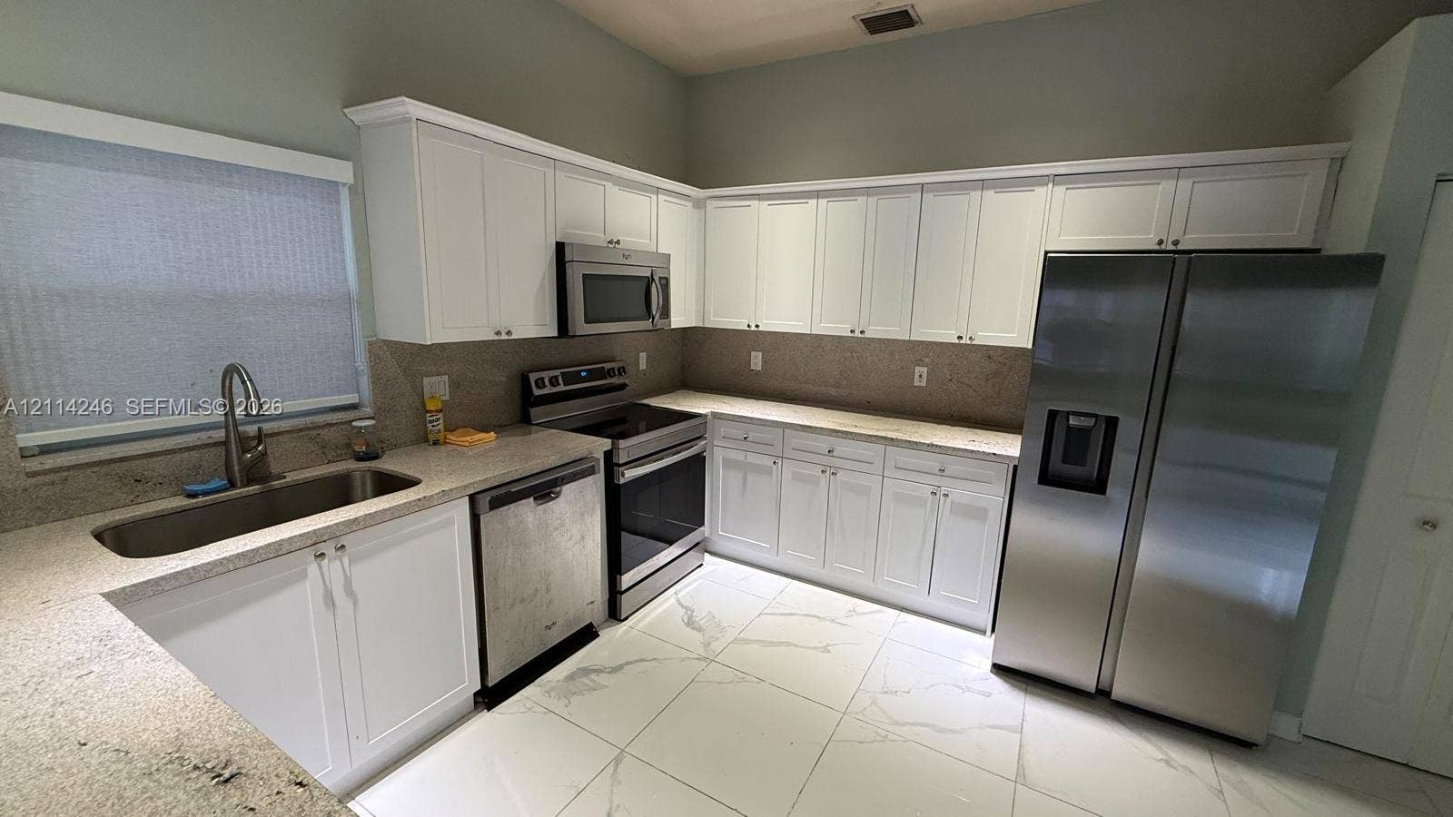 Kitchen featuring white cabinetry, stone-finish countertops, stainless steel appliances, a high-arc faucet, and large-format tile flooring