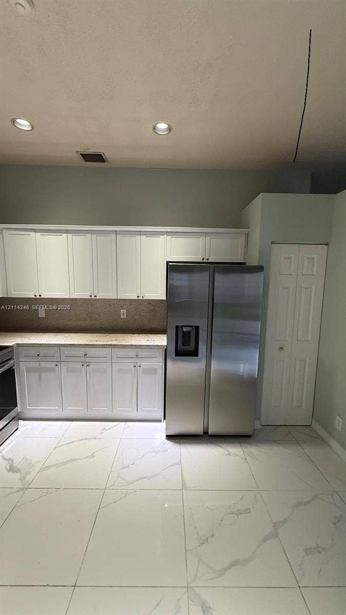 Kitchen featuring white cabinetry, stone-surface countertops, large-format tile flooring, stainless steel side-by-side refrigerator, and recessed ceiling lighting