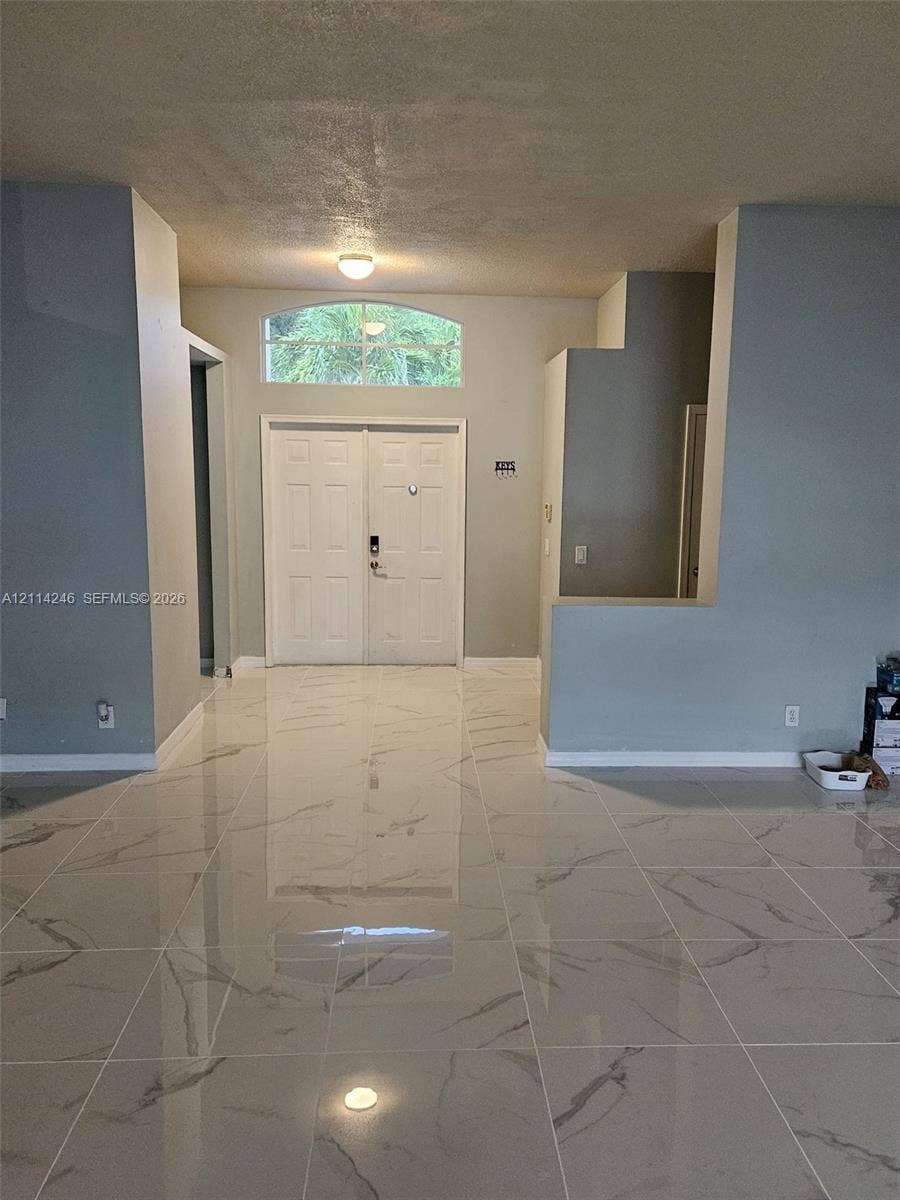 Double entry doors featuring a decorative arched transom window, finished with high-gloss large-format tile flooring and neutral-toned wall paint